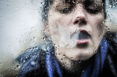 Close-up of woman emitting smoke on wet glass