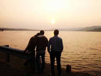 Full length of friends standing by lake against clear sky at sunset