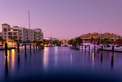 Boats moored in river against buildings in city at dusk