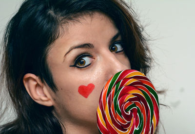 Portrait of young woman holding colorful lollipop against white background