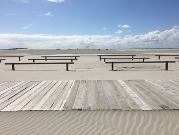 Empty benches with boardwalk on sand at beach against sky