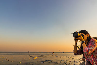 Woman photographing at beach during sunset