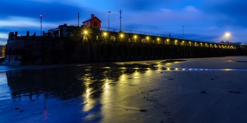 Illuminated bridge over river against sky at night