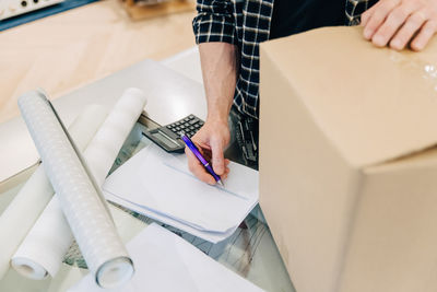 Midsection of salesman checking document by cardboard box in store