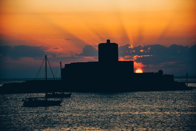 Silhouette sailboats in sea against orange sky