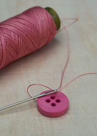 High angle view of pink thread with button and needle on table