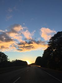 Road by silhouette trees against sky during sunset