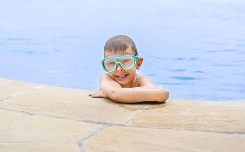 Cute boy wearing eyeglasses standing in swimming pool