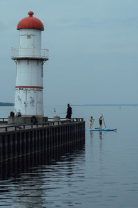 People on lighthouse by sea against sky