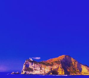 Rock formations in sea against clear blue sky