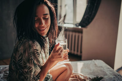 Young woman drinking from while sitting on bed at home