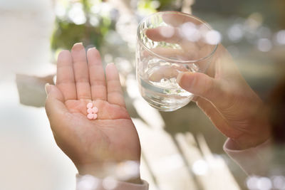 Cropped hands of woman holding pills and water in glass