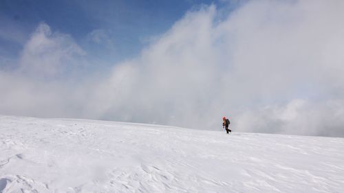 Person hiking on snow covered field against cloudy sky