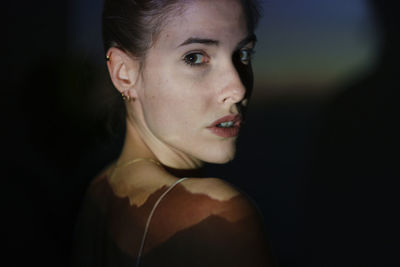 Close-up portrait of young woman against black background