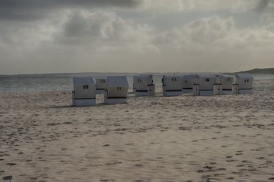 Hooded beach chairs on shore against sky