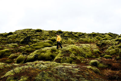 Man standing on rock looking at mountain against sky