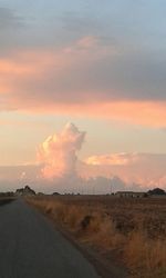 Road by field against sky during sunset