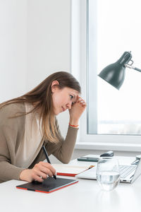Thoughtful girl sitting at the table with laptop and looking into screen. graphic designer.