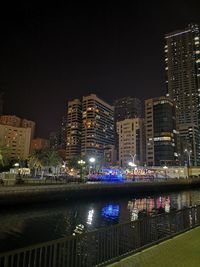 Illuminated buildings by river against sky at night