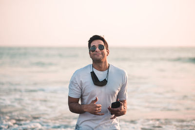 Portrait of young man wearing sunglasses while standing at beach