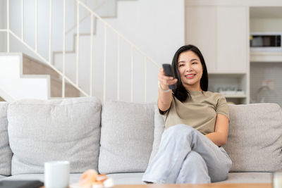 Young woman using mobile phone while sitting on sofa at home