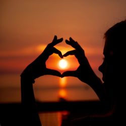 Silhouette woman making heart shape against sky during sunset