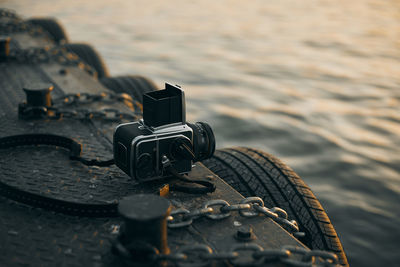 Close-up of camera against sea during sunset