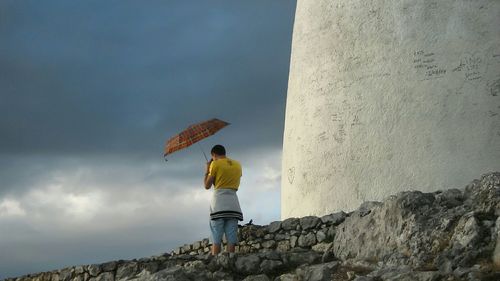 Low angle view of woman standing on rock against cloudy sky