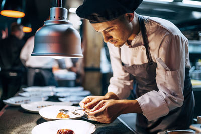 Side view of man in hat serving meal in restaurant kitchen