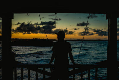 Silhouette of man looking at sea against sunset sky