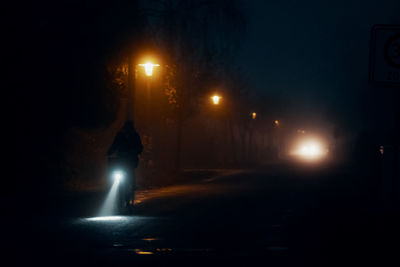 Person on bicycle on foggy illuminated street at night