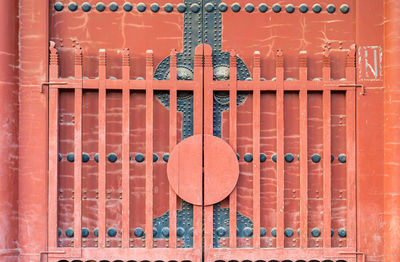 Close-up of metal fence against orange wall