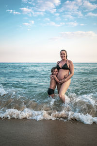 5 years old kid hugging pregnant mother, knee deep in the ocean