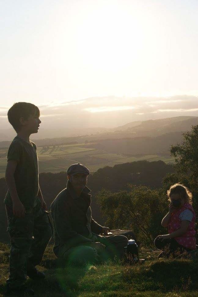 BOY SITTING ON LANDSCAPE AGAINST CLEAR SKY