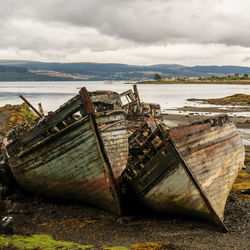 Abandoned boats moored at beach against sky