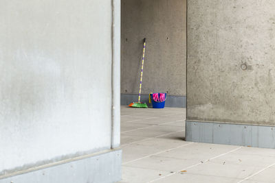 Multi colored broom with bucket on floor against wall seen from doorway