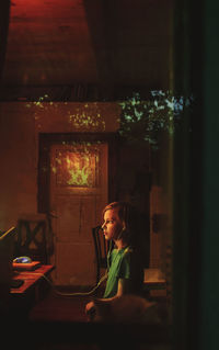 Side view through the window of a kid watching computer at the table at home. 