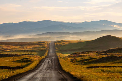 Countryroad at sunrise with hills and fog on the background