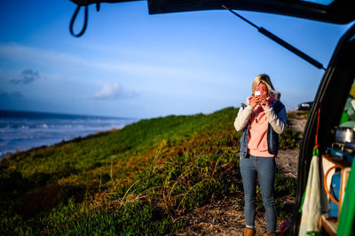 Woman photographing from mobile phone while standing by sea