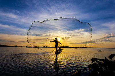 Silhouette man fishing in sea against sky during sunset