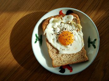 Directly above shot of fried egg on bread in plate at wooden table