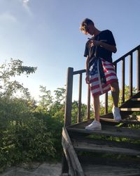 Boy standing by railing against sky