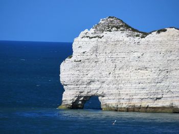 Rock formations in sea against clear blue sky