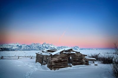 Built structure by frozen sea against sky during sunset