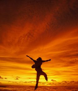 Silhouette man with arms outstretched jumping against orange sky