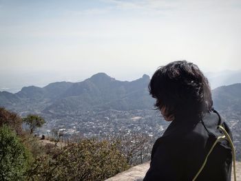 Man sitting on top of rock by mountains against clear sky