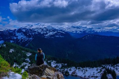 Rear view of hiker sitting on rock against snowcapped mountain