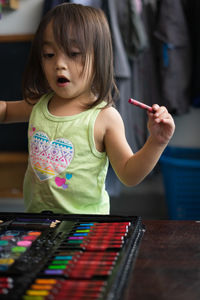 Cute girl by art and craft equipment on table at home