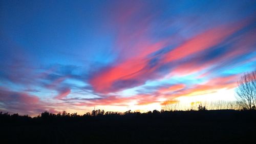 Silhouette of trees on landscape against cloudy sky