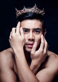 Close-up portrait of young man wearing crown against black background